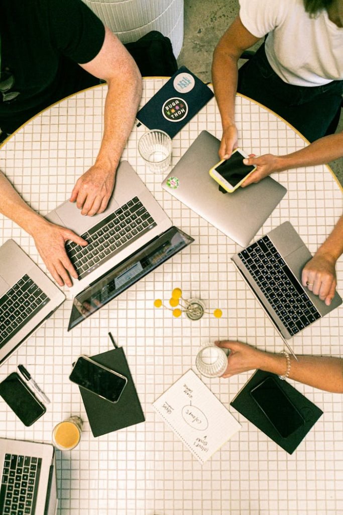 photo-of-people-using-laptop-3194519 Top view of a team collaborating with laptops, phones, and notes in a modern office.